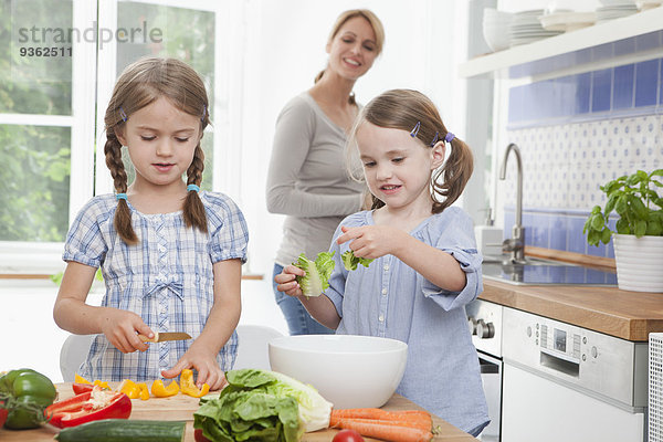 Deutschland  München  Mädchen (4-7) hacken Gemüse in der Küche  Mutter steht im Hintergrund