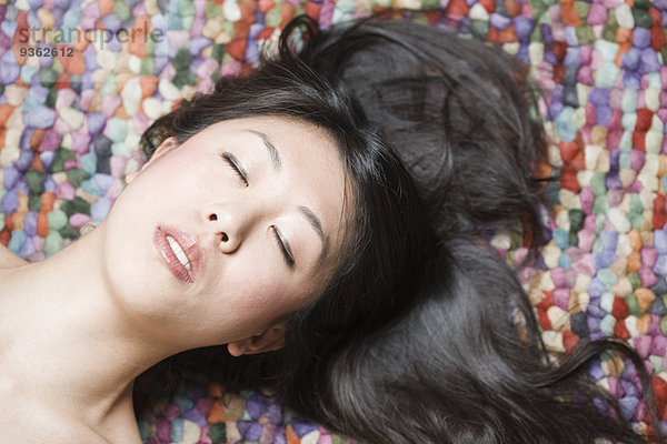Porträt einer Asiatin mit geschlossenen Augen vor farbigem Grund