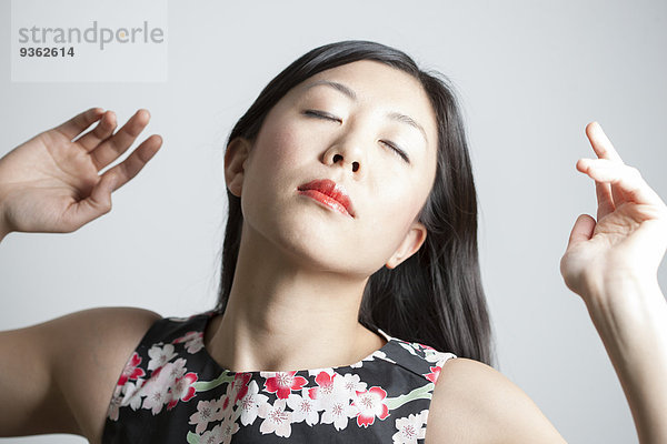 Porträt einer Asiatin mit geschlossenen Augen vor grauem Hintergrund
