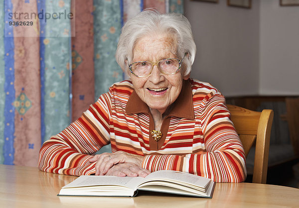 Porträt einer lächelnden Seniorin mit aufgeschlagenem Buch