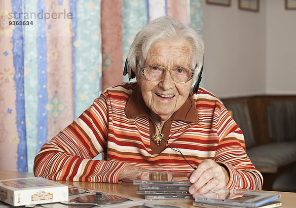 Porträt einer lächelnden Seniorin  die CDs mit Kopfhörern hört.