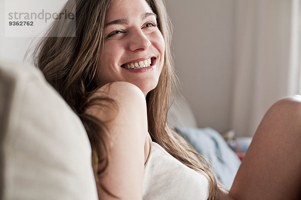 Porträt einer lächelnden jungen Frau auf der Couch in ihrem Wohnzimmer