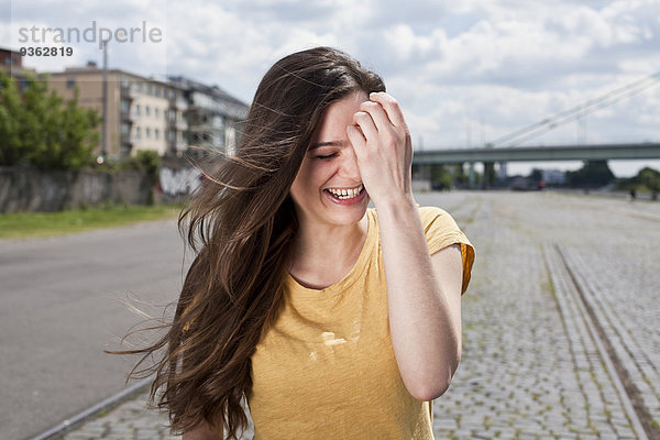 Deutschland  Nordrhein-Westfalen  Köln  Porträt der lachenden jungen Frau mit der Hand im Gesicht