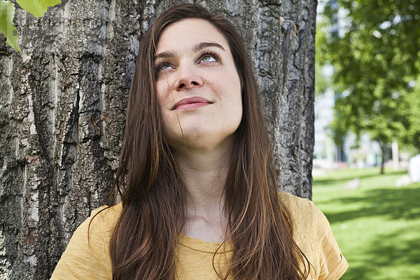 Porträt einer jungen Frau  die vor einem Baumstamm sitzt.