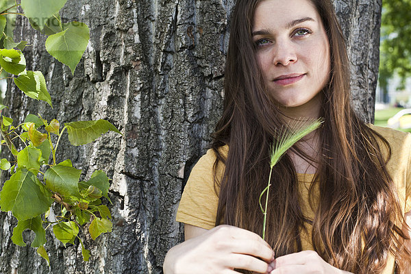 Bildnis einer jungen Frau mit Stachel in der Hand vor dem Baumstamm sitzend