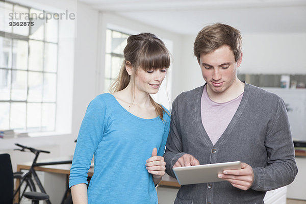 Zwei Kollegen stehen in einem Büro mit digitalem Tablett