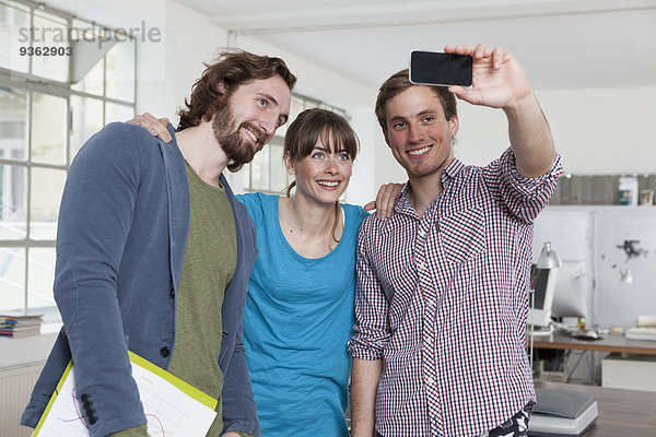 Drei Kollegen  die einen Selfie mit Smartphone in einem Büro nehmen