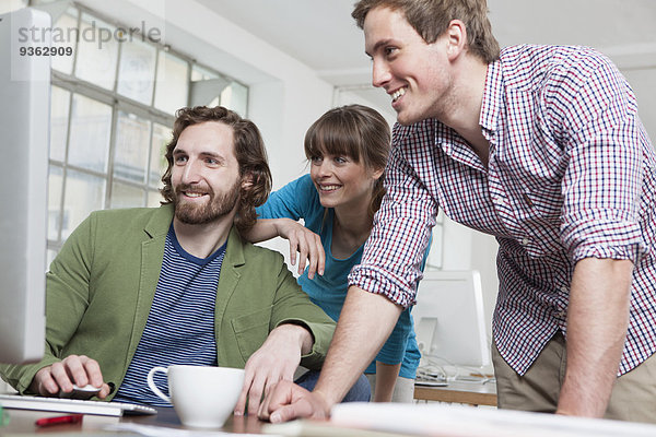 Drei Kollegen beim Blick auf den Computer in einem Kreativbüro