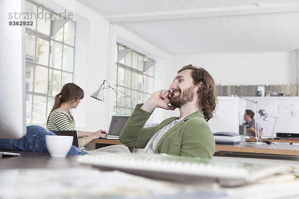 Junger Mann telefoniert an seinem Schreibtisch in einem Kreativbüro