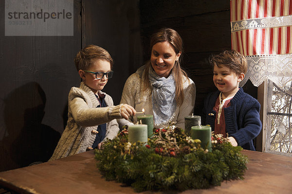 Mutter mit ihren zwei kleinen Söhnen entzündet Kerzen auf einem Adventskranz