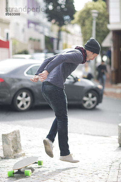 Junger Mann springt von seinem Skateboard auf einem Bürgersteig
