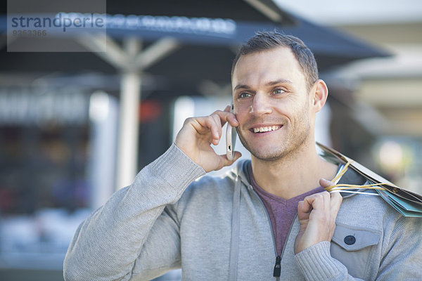 Porträt eines lächelnden Mannes mit Einkaufstaschen am Telefon