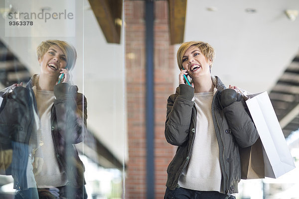 Porträt einer lachenden Frau  die vor einem Schaufenster telefoniert
