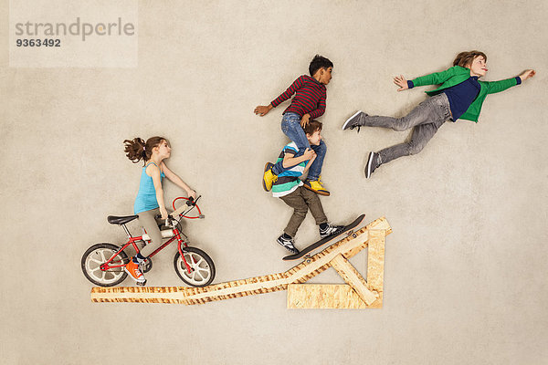 Kinder mit Fahrrad und Skateboard am Sprung