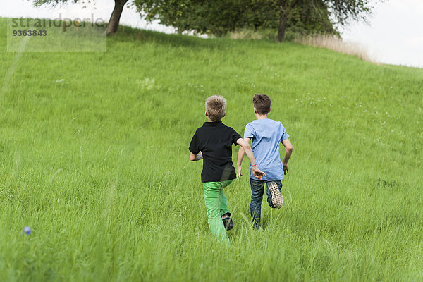 Zwei Jungen  die auf einer Wiese bergauf rennen.