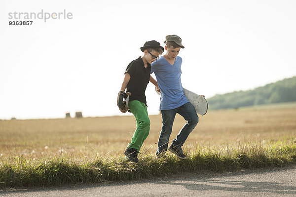 Zwei Jungen  die mit ihren Skateboards über ein Feld laufen.