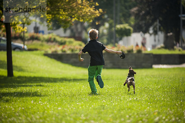 Junge rennt mit seinem Hund auf einer Wiese.