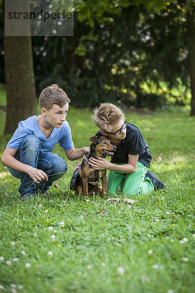 Zwei Jungen kauern mit ihrem Hund auf einer Wiese.