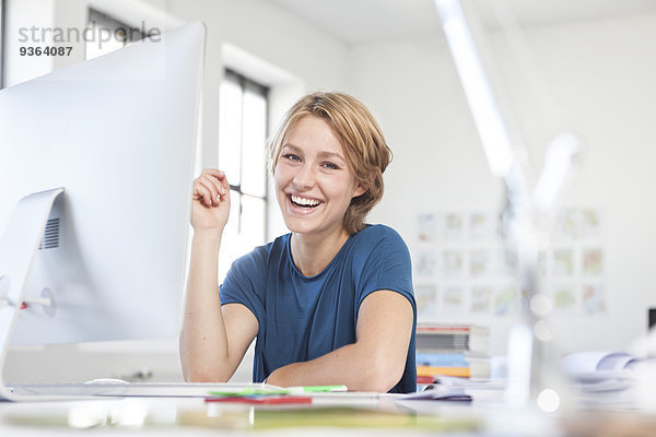 Porträt einer glücklichen jungen Frau an ihrem Schreibtisch in einem Kreativbüro