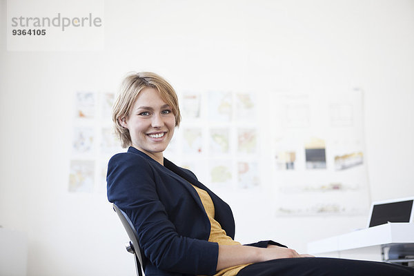 Porträt einer lächelnden jungen Frau an ihrem Schreibtisch in einem Kreativbüro