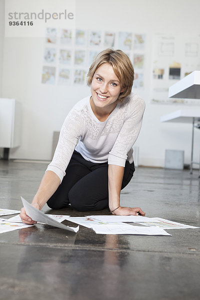 Porträt einer jungen Frau auf dem Boden eines Büros mit ihren Konzepten
