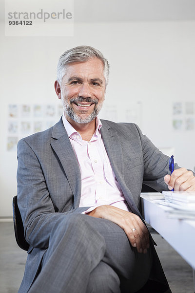 Porträt eines lächelnden Mannes an seinem Schreibtisch im Büro