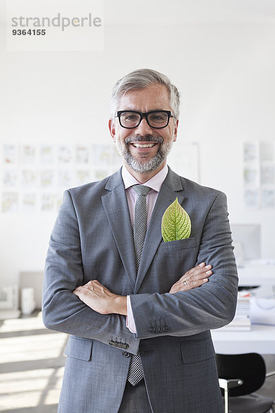 Porträt eines lächelnden Geschäftsmannes mit grünem Blatt in der Jackentasche