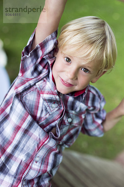 Porträt eines lächelnden kleinen Jungen beim Klettern auf Spielplatzgeräten