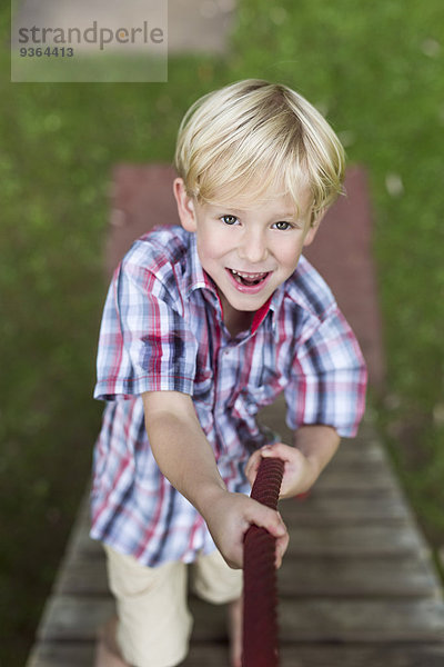 Porträt eines lächelnden kleinen Jungen beim Klettern auf einem Spielplatz