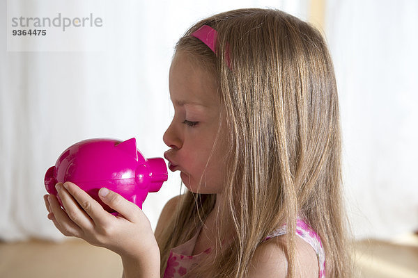 Kleines Mädchen  das sein rosa Sparschwein küsst.