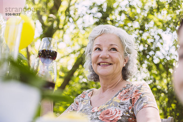 Lächelnde Seniorin mit einem Glas Rotwein im Garten