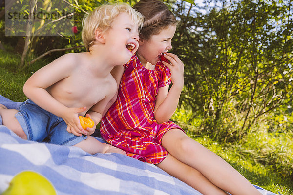 Junge und Mädchen genießen Obst auf Picknickdecke im Garten