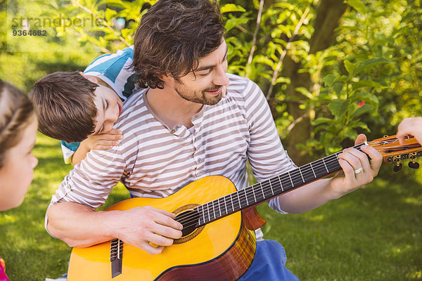 Vater mit Kindern beim Gitarrespielen im Garten