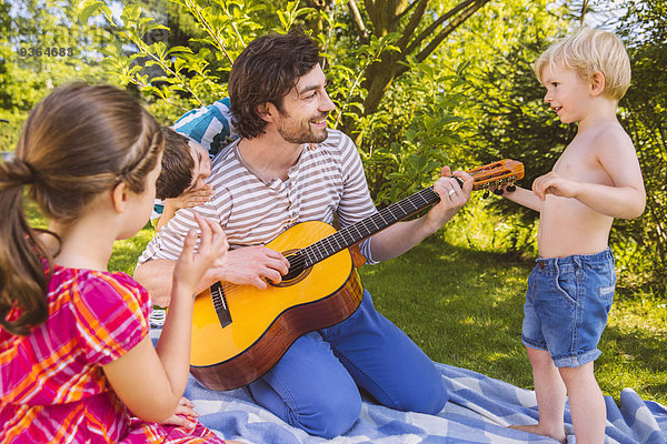 Vater mit Kindern beim Gitarrespielen im Garten