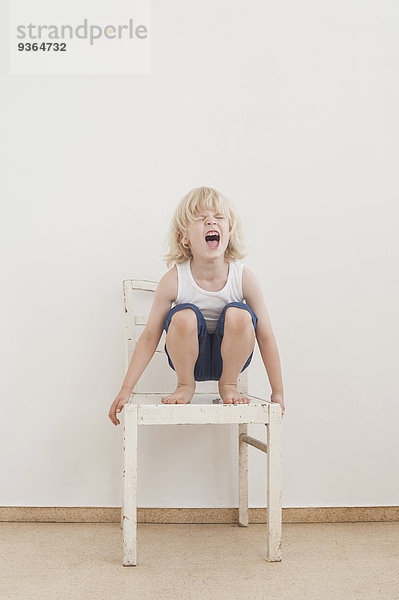 Porträt eines schreienden kleinen Jungen  der auf einem Stuhl krächzt.