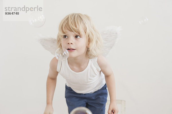 Porträt eines kleinen Jungen mit schrägen Flügeln  der Seifenblasen beobachtet.