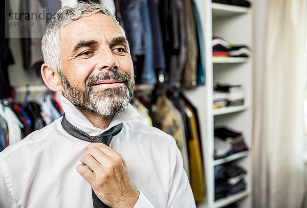 Porträt eines lächelnden Geschäftsmannes mit Krawatte an seinem begehbaren Kleiderschrank