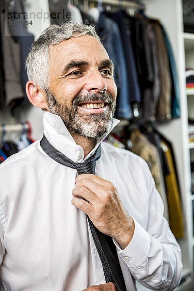 Porträt eines lächelnden Geschäftsmannes mit Krawatte an seinem begehbaren Kleiderschrank
