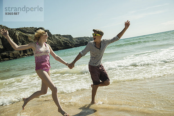 Teenager-Paar  das Hand in Hand am Wasser des Strandes läuft.