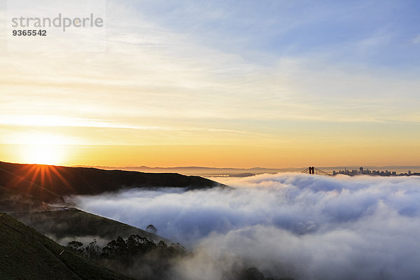 USA  Kalifornien  San Francisco  Skyline und Golden Gate Bridge im Nebel bei Sonnenaufgang vom Hawk Hill aus gesehen.