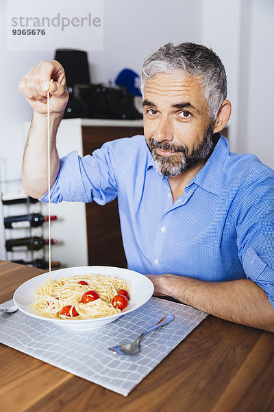 Porträt eines Mannes  der in seiner Küche Pasta isst.