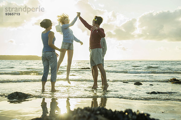 Frau und drei Teenager am Strand bei Sonnenuntergang
