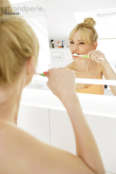 Frau schaut beim Zähneputzen auf ihr Spiegelbild