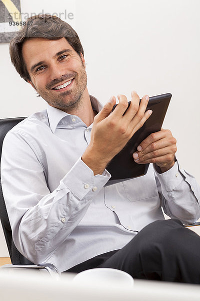 Lächelnder junger Geschäftsmann mit Tablet-Computer im Büro
