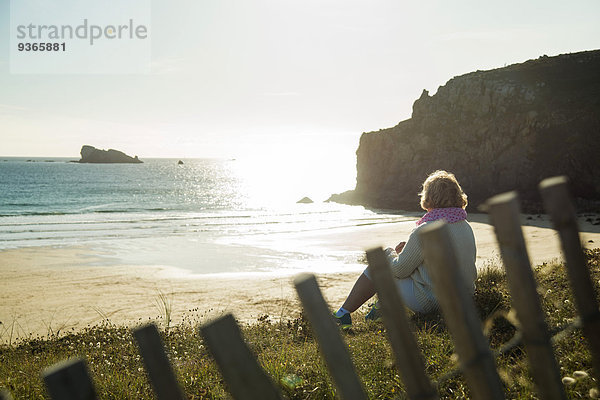 Frankreich  Bretagne  Camaret-sur-Mer  Seniorin an der Küste sitzend