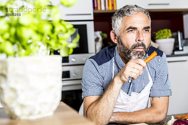 Österreich  Mann in der Küche isst Karotte