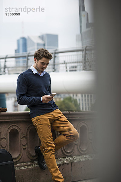 Deutschland  Hessen  Frankfurt  junger Mann auf einer Brücke stehend mit Smartphone