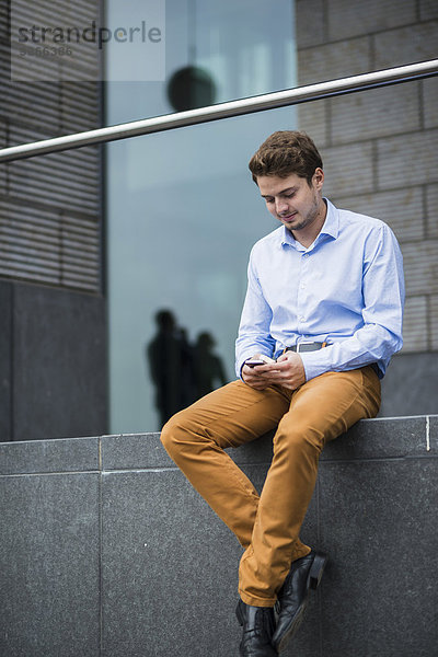 Deutschland  Hessen  Frankfurt  Portrait eines sitzenden jungen Mannes mit seinem Smartphone