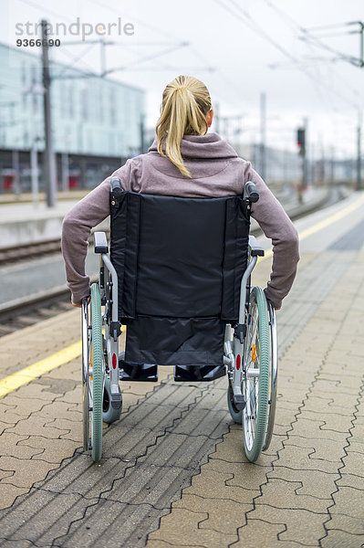 Frau im Rollstuhl am Bahnsteig wartend