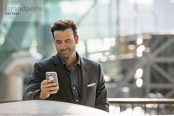 Ein Mann sitzt auf einer Bank und überprüft sein Smartphone.